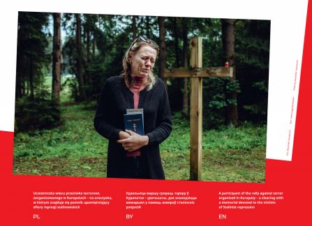 Photograph from the exhibition Belarus. road to freedom. participant in a protest in Kuropaty at the monument to the victims of Stalinist repression. a weeping woman holding the New Testament, besides her a wooden cross, in the background a forest.